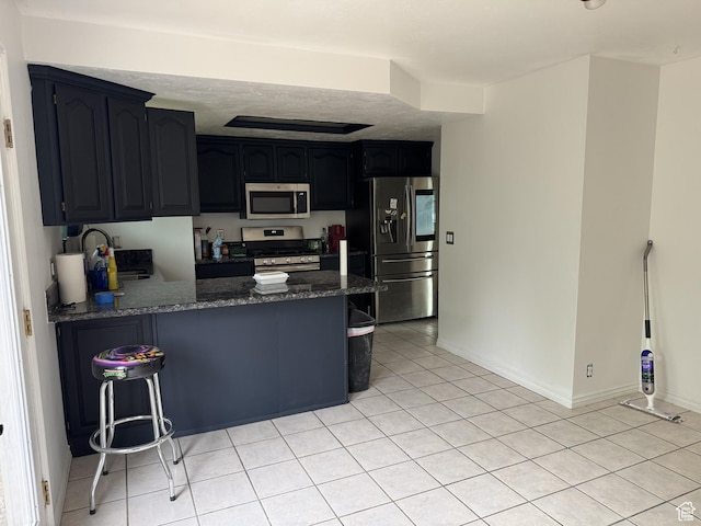 5488 S Hollow Springs Cir W, Murray, UT 84123 - kitchen with stainless steel appliances, a peninsula, dark stone counters, light tile patterned floors, and a kitchen bar