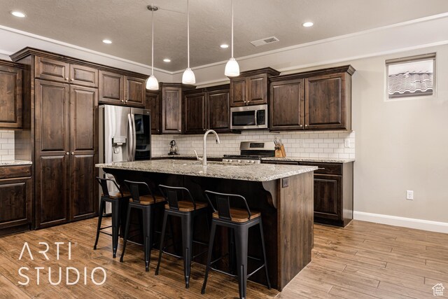 2691 E 3800 S, St George, UT 84790 - kitchen with light wood finished floors, a breakfast bar, a center island with sink, stainless steel appliances, and visible vents