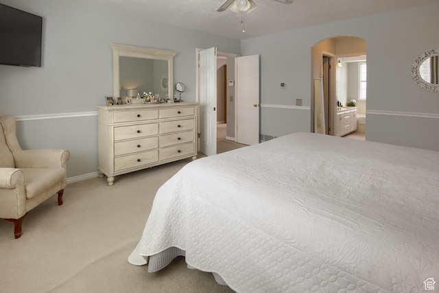 bedroom with a ceiling fan, light colored carpet, arched walkways, baseboards, and connected bathroom