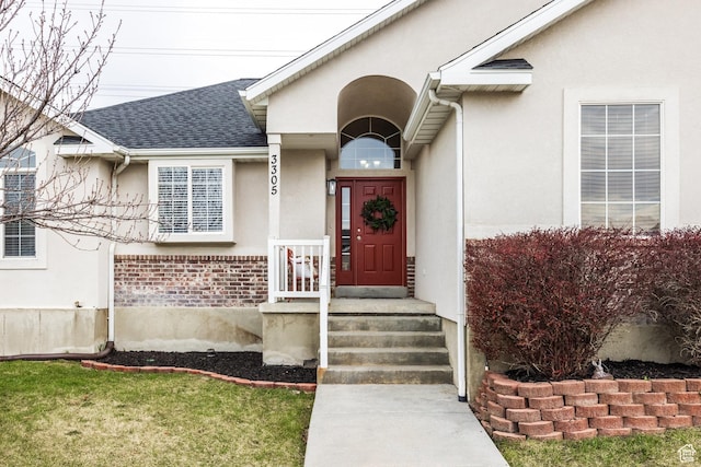 entrance to property with roof with shingles, brick siding, and stucco siding