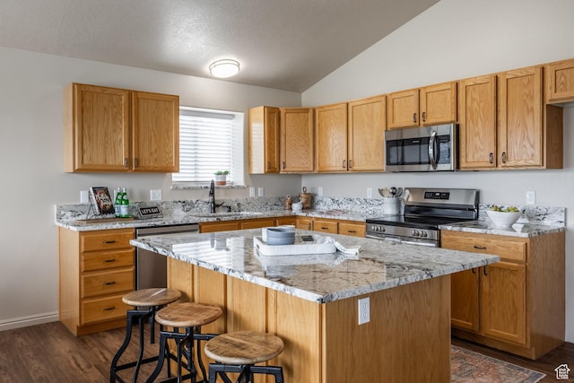 kitchen with vaulted ceiling, a sink, stainless steel appliances, a kitchen bar, and dark wood-type flooring