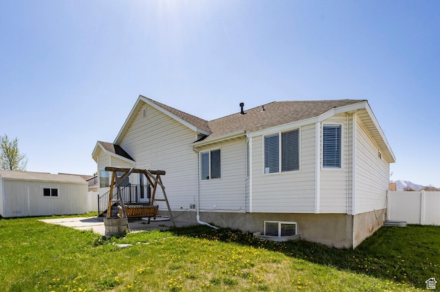 back of house featuring an outdoor structure, a lawn, fence, and roof with shingles