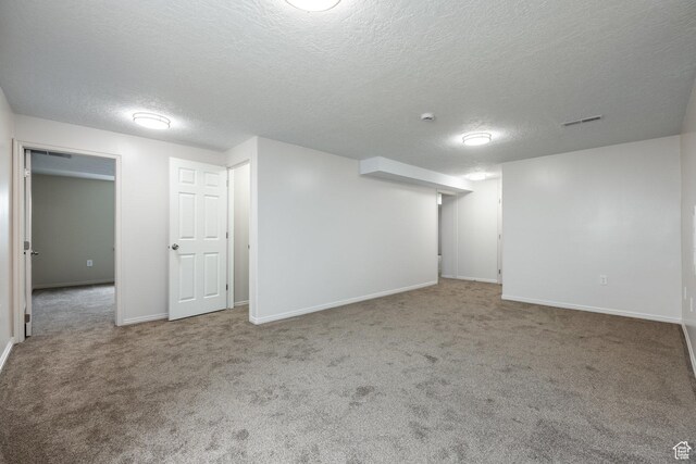 finished basement featuring visible vents, baseboards, carpet flooring, and a textured ceiling