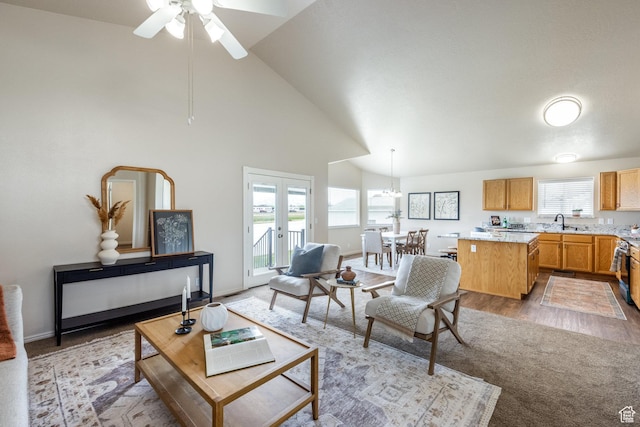 living room featuring high vaulted ceiling, baseboards, light wood-type flooring, and ceiling fan with notable chandelier