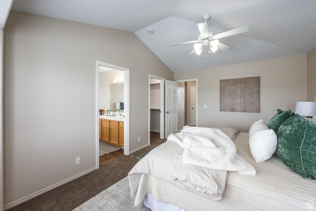 bedroom featuring dark carpet, vaulted ceiling, a walk in closet, baseboards, and ensuite bathroom