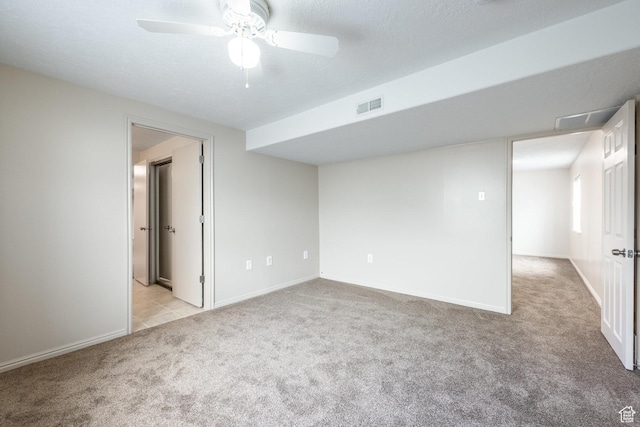 spare room featuring light carpet, a ceiling fan, visible vents, and baseboards