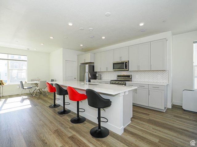 10638 S Pipestone Way W Unit 136, South Jordan, UT 84009 - kitchen with appliances with stainless steel finishes, a sink, dark wood-style flooring, an island with sink, and tasteful backsplash