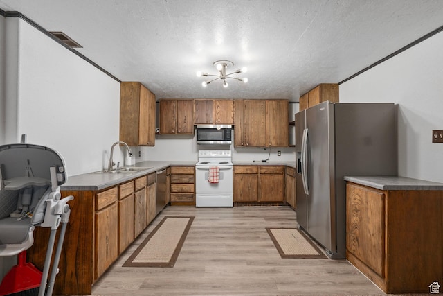 kitchen featuring an inviting chandelier, a sink, appliances with stainless steel finishes, brown cabinetry, and light wood finished floors
