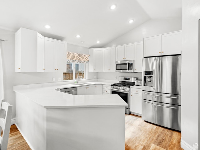 kitchen featuring a sink, light wood finished floors, a peninsula, stainless steel appliances, and white cabinets