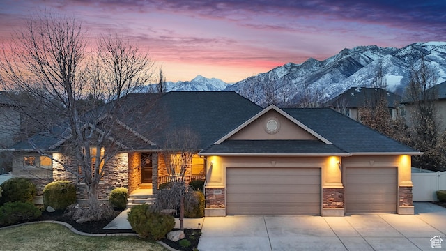 view of front of house featuring a mountain view, stone siding, a garage, stucco siding, and driveway