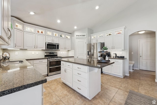 kitchen featuring white cabinetry, a kitchen island, appliances with stainless steel finishes, arched walkways, and a sink