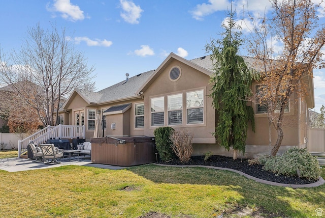 rear view of property featuring a hot tub, a lawn, fence, a patio, and stucco siding