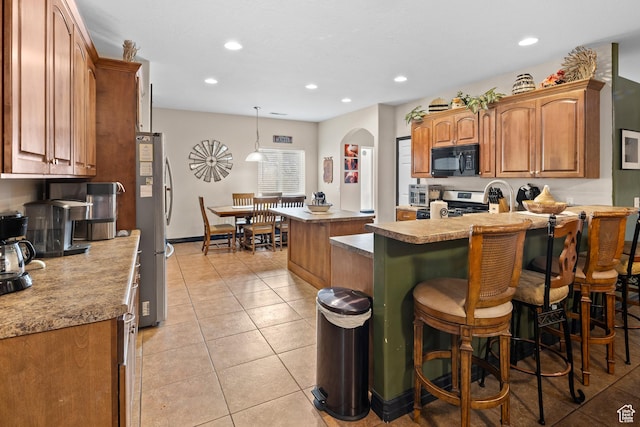 98 E Mt Peale Dr, Moab, UT 84532 - kitchen with light tile patterned floors, a breakfast bar, a kitchen island, arched walkways, and appliances with stainless steel finishes