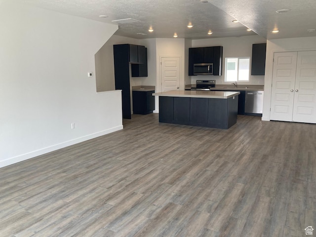 kitchen featuring light countertops, a sink, a kitchen island, appliances with stainless steel finishes, and dark wood finished floors