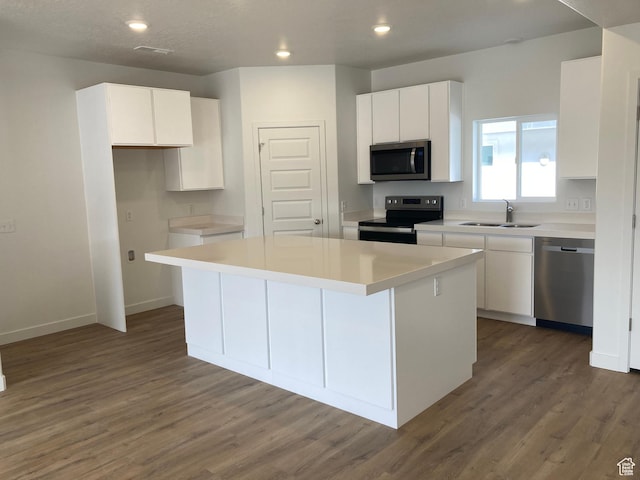 kitchen with white cabinets, wood finished floors, a kitchen island, appliances with stainless steel finishes, and a sink