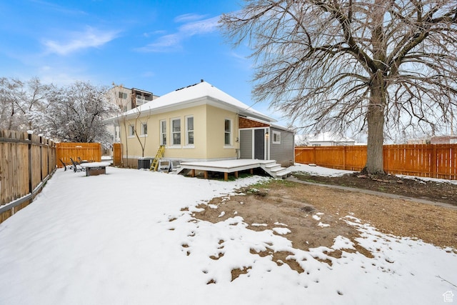 snow covered rear of property with a fenced backyard and a wooden deck