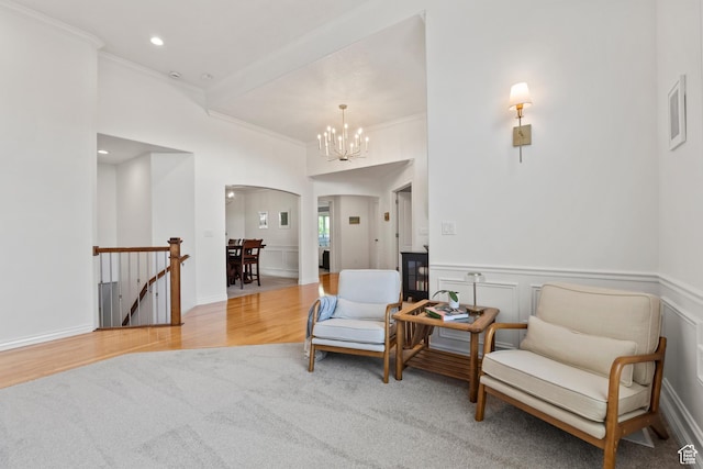 living area with an upstairs landing, arched walkways, crown molding, a chandelier, and wood finished floors