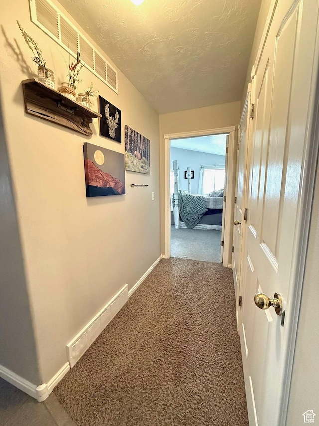 hallway featuring carpet flooring, a textured ceiling, and baseboards