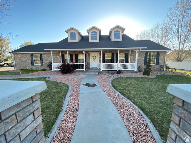 cape cod home featuring a porch, a front yard, fence, brick siding, and a shingled roof