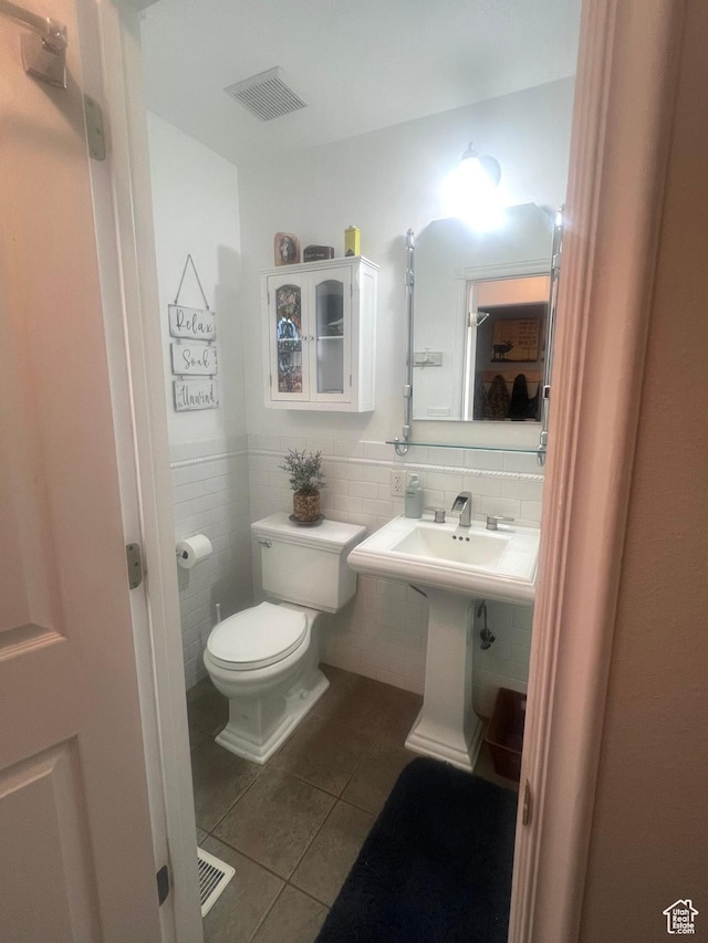 half bath with tile patterned floors, toilet, visible vents, wainscoting, and tile walls