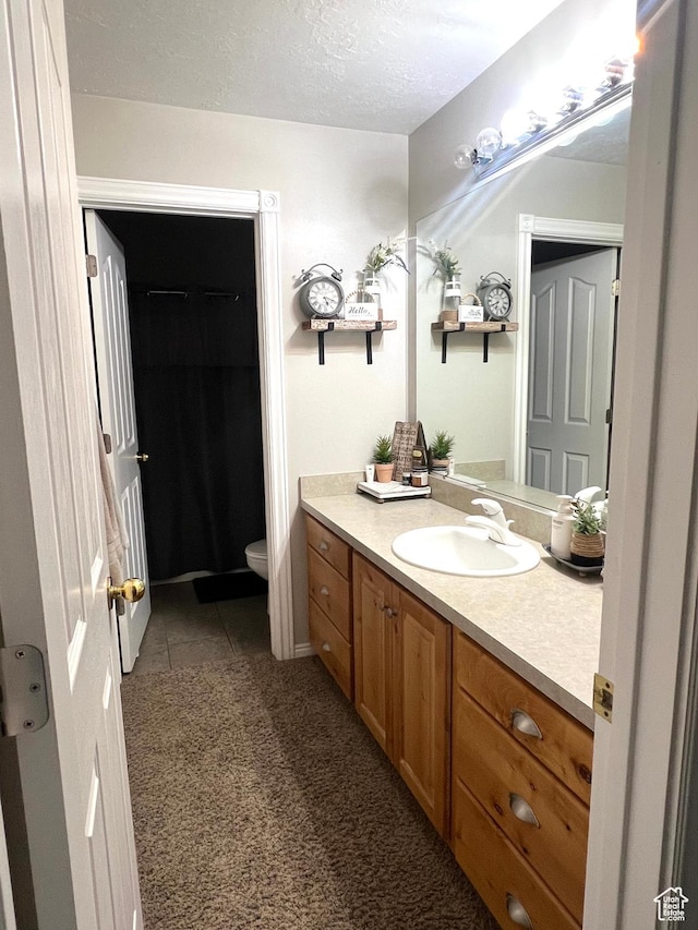 bathroom with tile patterned floors, vanity, a textured ceiling, and toilet