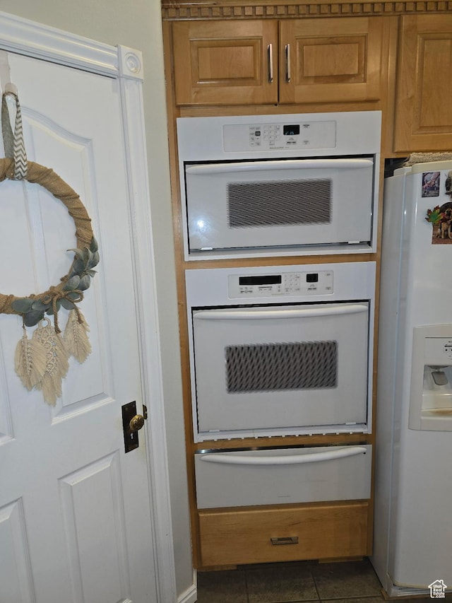 kitchen with a warming drawer, brown cabinets, white appliances, and tile patterned flooring