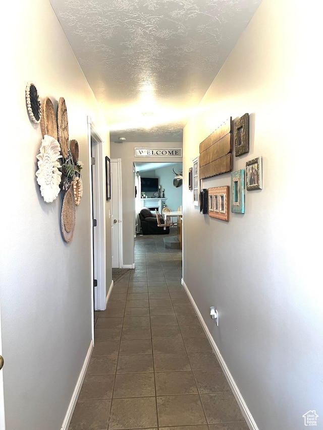 corridor with dark tile patterned floors, baseboards, and a textured ceiling