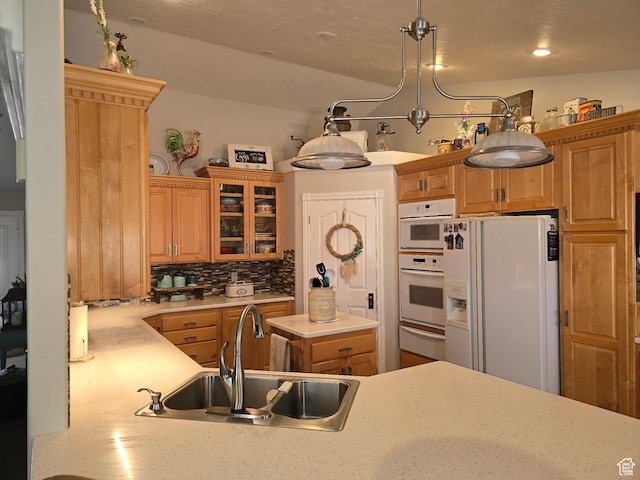 kitchen featuring tasteful backsplash, white appliances, glass insert cabinets, light countertops, and a sink