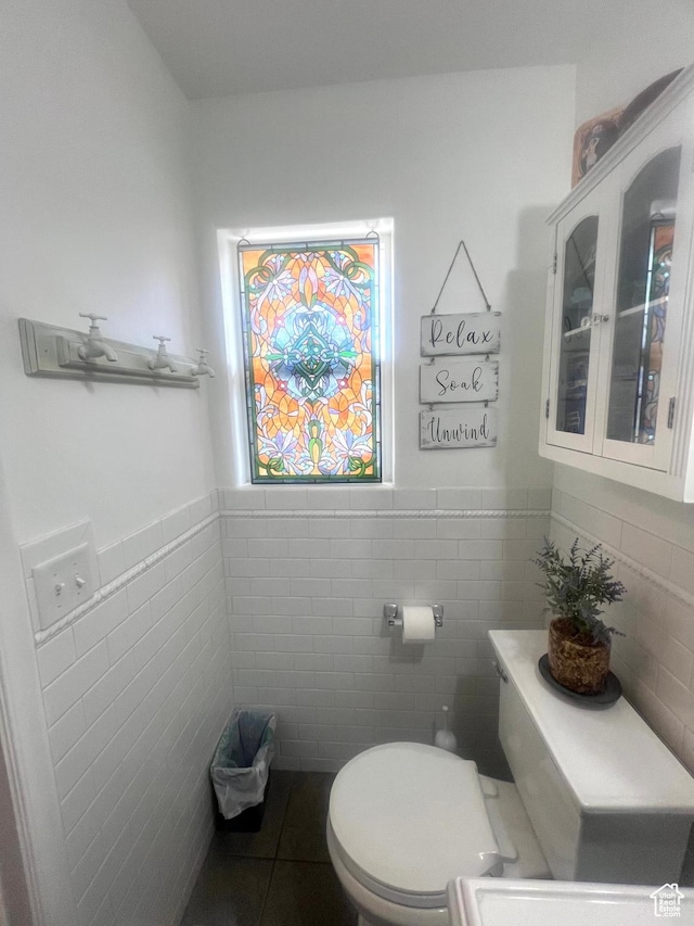 half bath featuring tile patterned floors, toilet, tile walls, and wainscoting