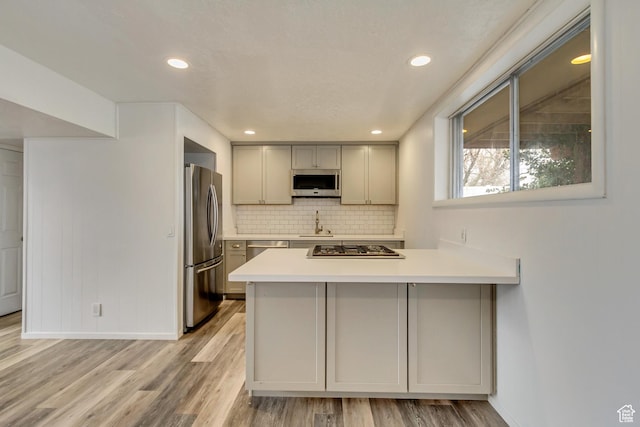 1055 E Chevy Chase Dr S, Murray, UT 84117 - kitchen with light countertops, a peninsula, appliances with stainless steel finishes, gray cabinetry, and backsplash