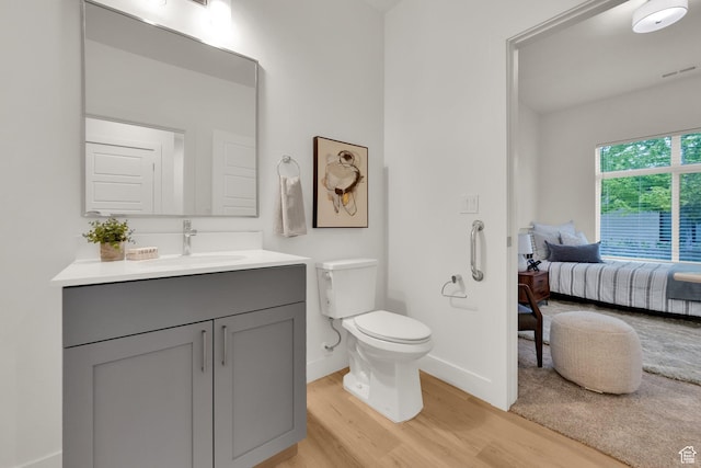 bathroom with wood finished floors, toilet, vanity, baseboards, and ensuite bath