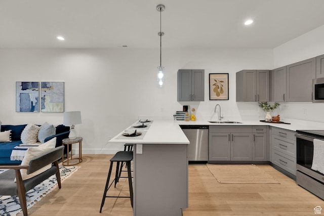 kitchen featuring appliances with stainless steel finishes, gray cabinets, a peninsula, a sink, and light wood-style floors