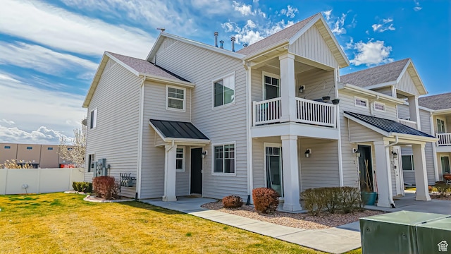 view of front of home featuring a balcony, metal roof, fence, a standing seam roof, and a front lawn