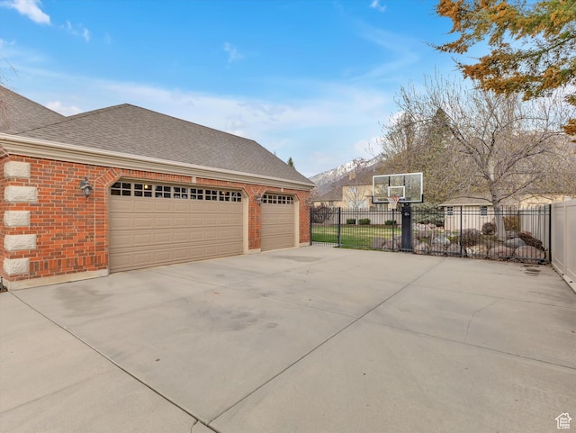 exterior space with concrete driveway, brick siding, fence, and a shingled roof