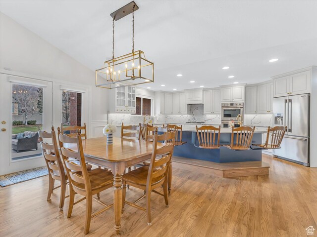 dining area featuring a chandelier, lofted ceiling, light wood-style floors, a decorative wall, and recessed lighting