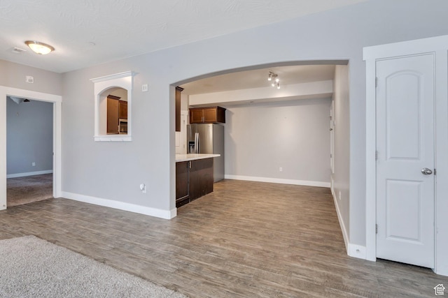 unfurnished living room featuring wood finished floors, baseboards, and arched walkways