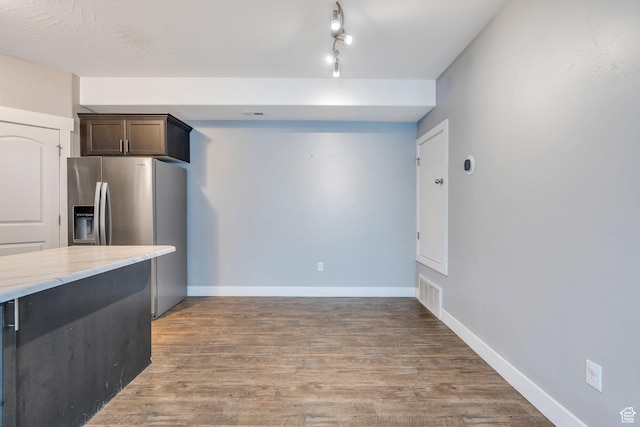 kitchen with stainless steel fridge with ice dispenser, dark brown cabinetry, wood finished floors, and light stone counters