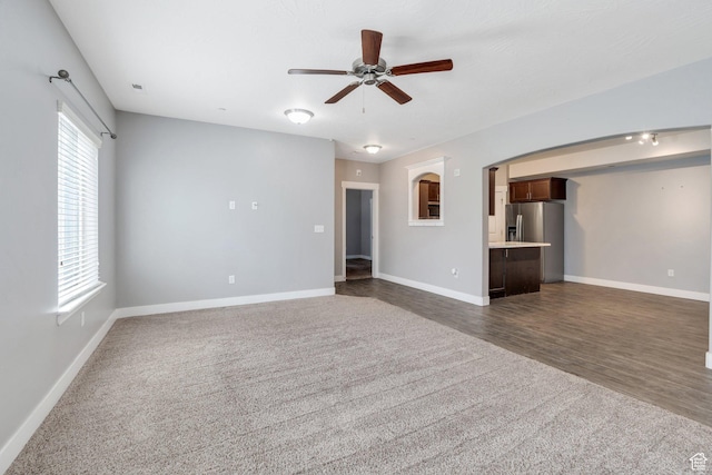 unfurnished living room with a ceiling fan, dark carpet, and baseboards