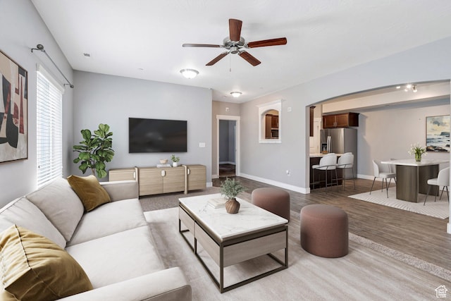living room with a ceiling fan, baseboards, wood finished floors, and arched walkways
