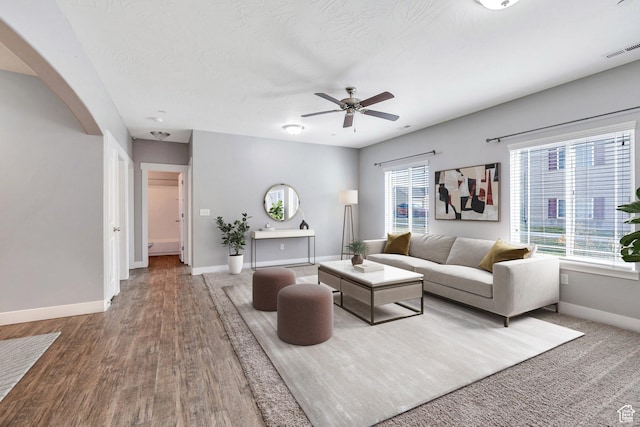 living area featuring baseboards, a ceiling fan, wood finished floors, and arched walkways