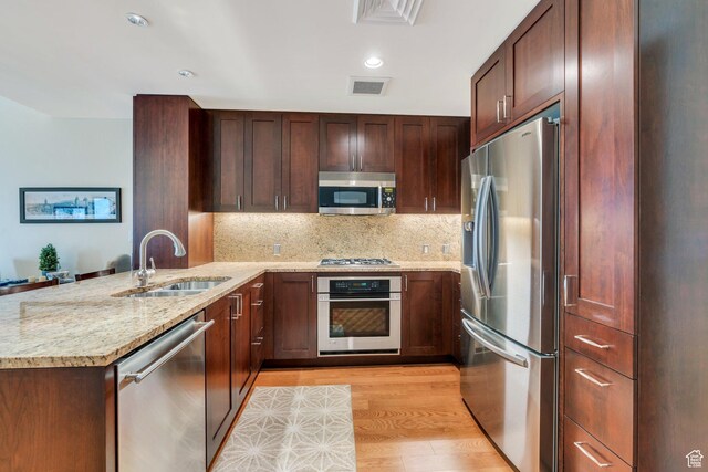 45 W S Temple Unit 603, Salt Lake City, UT 84101 - kitchen with light wood-style flooring, a peninsula, light stone countertops, stainless steel appliances, and a sink