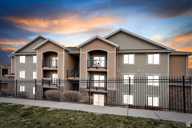 view of front of house featuring stucco siding, a balcony, and a fenced front yard