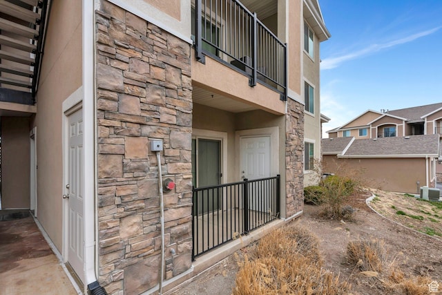 entrance to property featuring stone siding, a balcony, and stucco siding