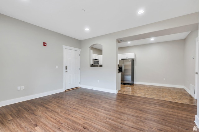 unfurnished room with dark wood-style flooring, arched walkways, baseboards, and recessed lighting