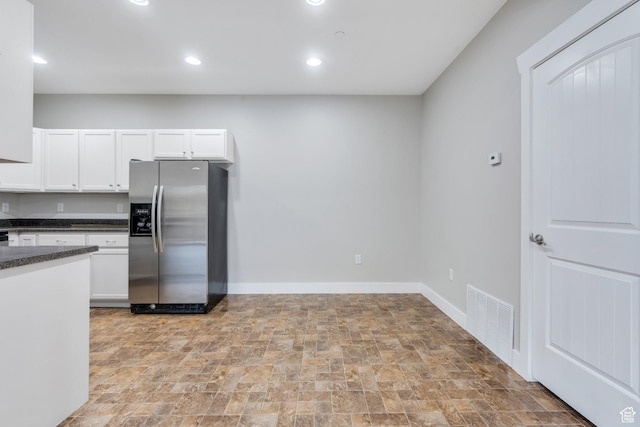 kitchen featuring stainless steel fridge, dark countertops, stone finish floors, white cabinetry, and baseboards