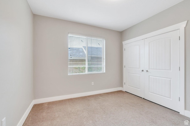 unfurnished bedroom with light carpet, baseboards, and a closet