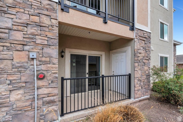 view of exterior entry with stone siding, stucco siding, and a balcony