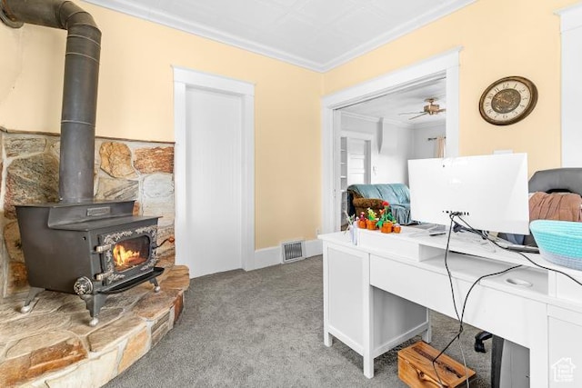 carpeted home office with crown molding, a wood stove, and visible vents