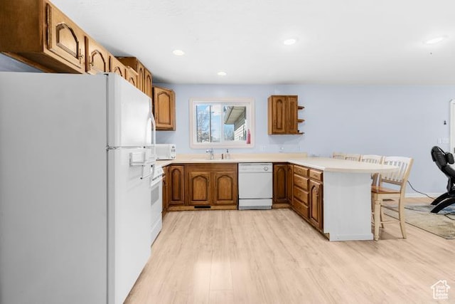 kitchen featuring a peninsula, white appliances, brown cabinets, light wood-type flooring, and a kitchen breakfast bar