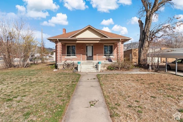 bungalow-style house with a front lawn, a chimney, covered porch, and brick siding